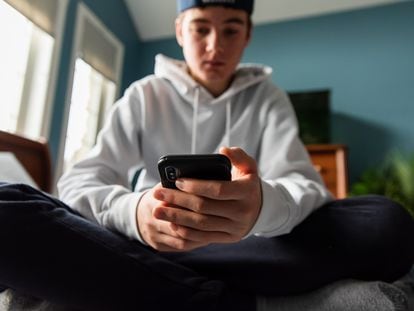 Un adolescente consulta su 'smartphone', sentado en su cuarto.