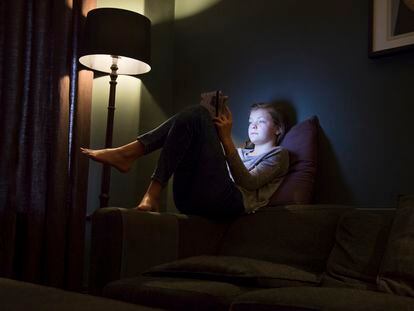 Una adolescente mira su tableta en la cama.