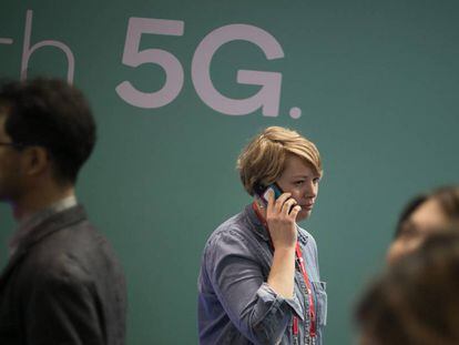 Una mujer camina mientras habla por telefono mientras pasa junto a un anuncio de tecnologia 5G.