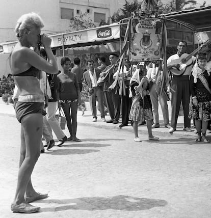 Una turista en biquini fotografía una procesión festiva de la Agrupación musical Rondalla, La Veterana, en Benidorm, en 1964. |