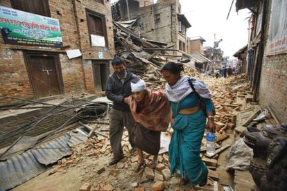 Un dona gran camina, ajudada per dues persones, pels carrers de Bhaktapur, prop de Kathmandú, després d'haver d'abandonat casa seva.