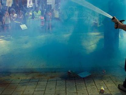 Un bombero riega a los manifestantes, envueltos en una cortina de humo.