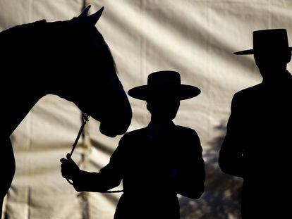 Dos jinetes dialogan mientras sujetan por la rienda a un caballo.