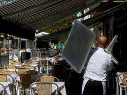 Un camarero recoge una mesa de una terraza de un restaurante del barrio de la Barceloneta de Barcelona.