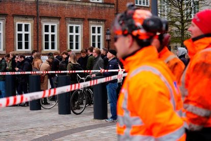 Ciudadanos y personal de emergencia contemplan el incendio del edificio detrás de una zona demarcada, este martes. 