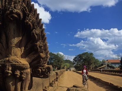 Una mujer pedalea por el Spean Praptos, el puente más impresionante de la ruta de los puentes angkorianos, con gigantescas ‘nagas’ (cobras) de piedra que amparan la imagen de Buda.
