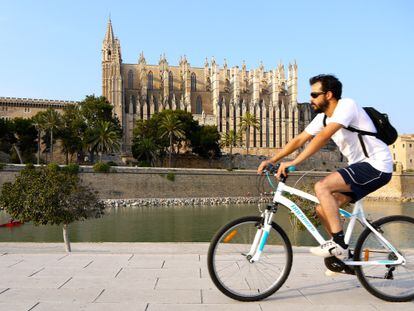 Un joven circula con su bicicleta junto a la catedral de Palma.