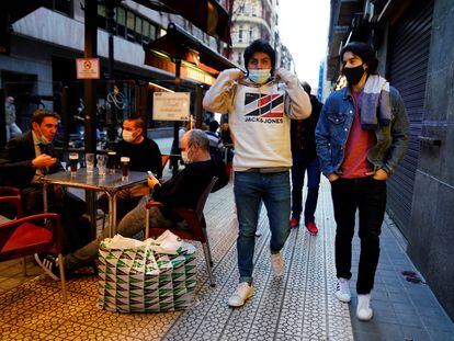 Varios jóvenes con mascarilla pasan ante los clientes de un bar en el centro de Bilbao.