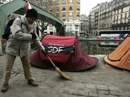 Un indigente barre la acera junto al campamento que Los Hijos de Don Quijote han instalado en el canal Saint Martin en París.