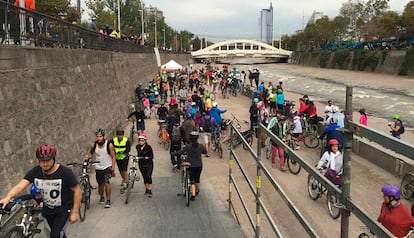 Decenas de personas caminan y andan en bicicleta a lo largo de un río rehabilitado en Santiago de Chile.