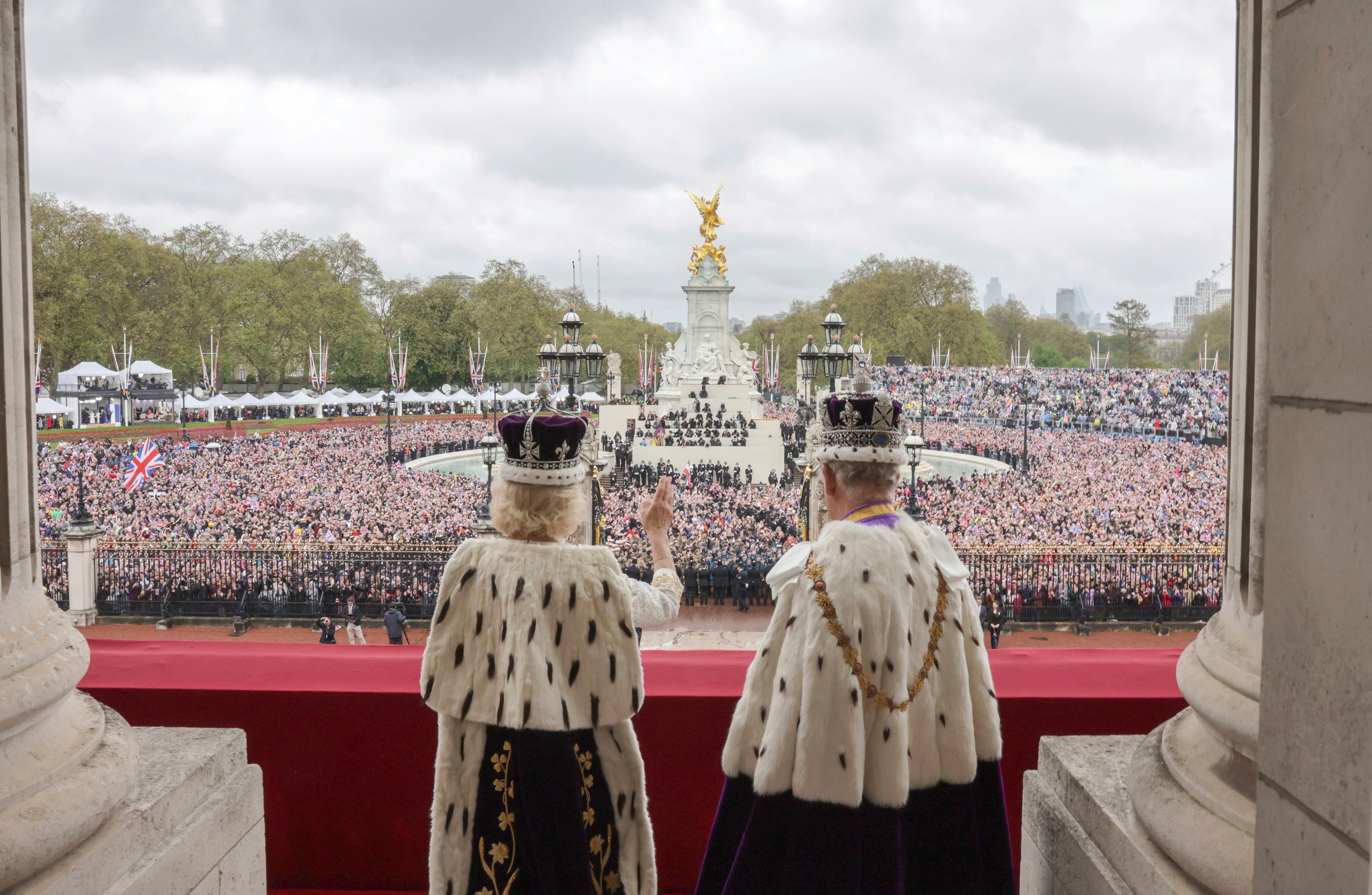 Carlos III y la reina Camila saludan al público congregado a las puertas del palacio de Buckingham. 