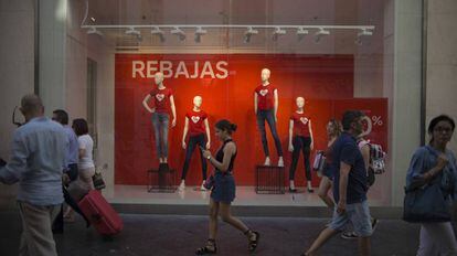 Una joven consulta en Sevilla el móvil frente a un comercio en temporada alta de ventas y contratación temporal.