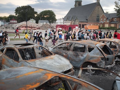 Un grupo de manifestantes pacíficos pasa junto a unos coches quemados en Kenosha.