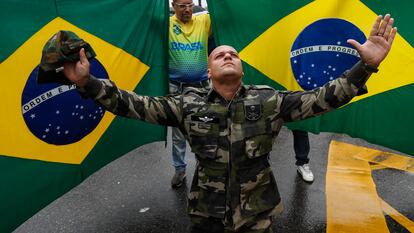 Jair Bolsonaro supporter wearing military clothes, kneeling in front of two Brazilian flags during Rio De Janeiro protests