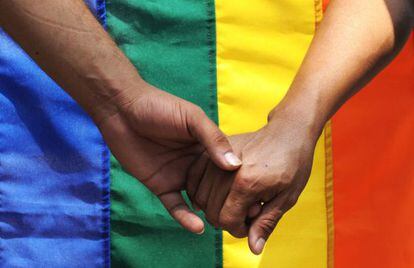 Dos hombres de la mano ante una bandera gay. 