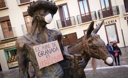 Una de las estatuas de Granada, con mascarillas y un cartel colgado. 