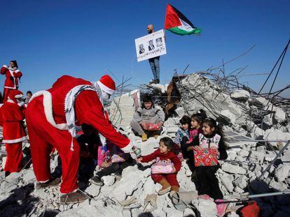 Un manifestate palestino vestido de Papá Noel entrega regalos a unos niños en los restos de una casa demolida por Israel en Belén.