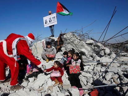 Un manifestate palestino vestido de Papá Noel entrega regalos a unos niños en los restos de una casa demolida por Israel en Belén.