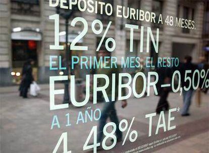 Viandantes reflejados en un escaparate de una entidad bancaria, en Bilbao, con una oferta de depósitos.