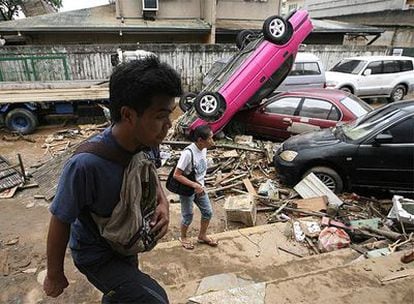 Ciudadanos filipinos pasan al lado de coches dañados por las inundaciones en la ciudad de Marikina.