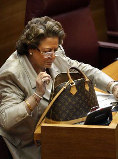 Rita Barberá busca algo en su bolso que lleva estampada la marca Louis Vuitton en un pleno de las Cortes.