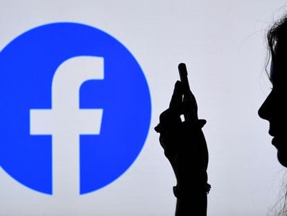 Un usuario navega con su teléfono móvil sobre un fondo con el logo de Facebook.