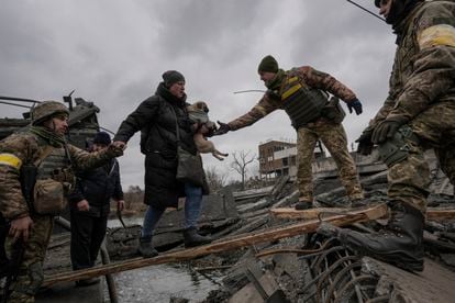 Militares ucranios ayudan a una mujer con un perro pequeño a cruzar el río Irpin por un camino improvisado bajo un puente destruido por un ataque aéreo ruso.