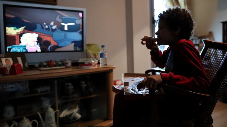 Un niño come un trozo de pizza mientras ve la televisión en Madrid.