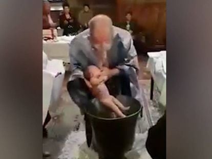 Un párroco introduce el cuerpo de un bebé en la pila bautismal.