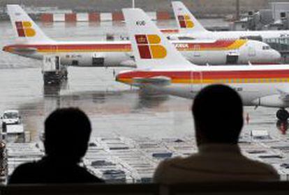 Dos pasajeros observan varios aviones de la compa&ntilde;ia Iberia en las pistas del aeropuerto de Barajas.