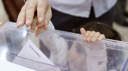 Un padre empuja el voto con el dedo de su pequeña hija en el colegio electoral en Madrid.