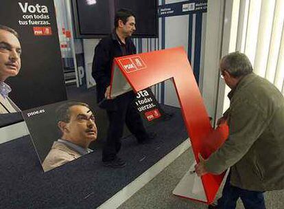 Dos operarios colocan el atril emblemático de los mítines de Zapatero durante la presentación de la cartelería de la campaña en la sede del PSOE.