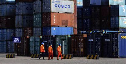 Tres empleados caminan entre los contenedores del puerto de Qingdao, China. 