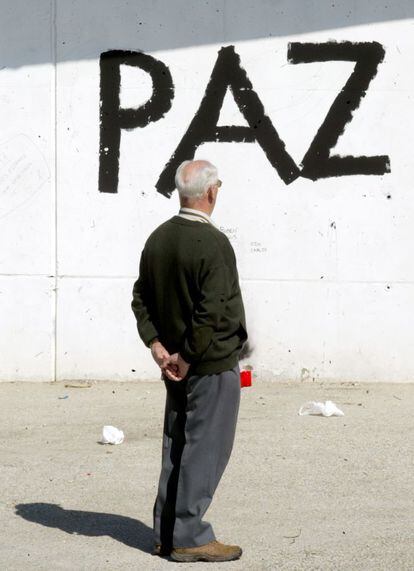 Un hombre observa una pintada en favor de la paz hecha en el muro de la estación de Cercanías de El Pozo, en señal de duelo por las víctimas. El 14-M, en el cementerio de la Almudena todavía quedan cadáveres sin identificar.
