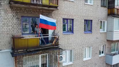 Un hombre coloca una bandera nacional rusa en un balcón de un edificio residencial en Lisichansk, en una imagen distribuida por el Ministerios de Defensa ruso.