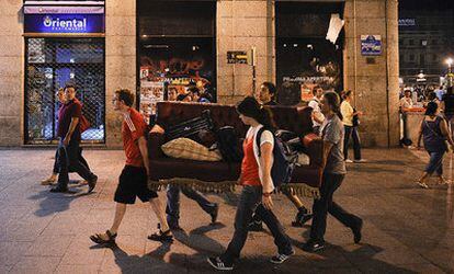 Varios jóvenes transportan por la calle del Carmen uno de los sofás del campamento de Sol.