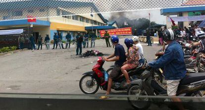 Motoristas pasan ante los policías que vigilan la zona donde se encuentra una factoría incendiada en la provincia vietnamita de Binh Duong.