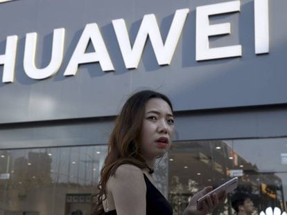 Una mujer usa un teléfono móvil junto a un establecimiento de Huawei en Pekín
