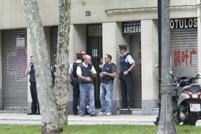 Agentes de los Mossos'd Esquadra custodian la entrada del edificio en el que se mantiene atrincherado el hombre que ha disparado a un compañero de piso en Barcelona.