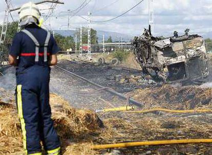 Un bombero trabaja en la extinción del fuego producido al ser arrollado un camión cargado de paja (cuya cabina se ve a la derecha) por el tren que cubría el trayecto Oviedo-Barcelona (al fondo), al paso por la aldea de Margarita, en el municipio de Vitoria.