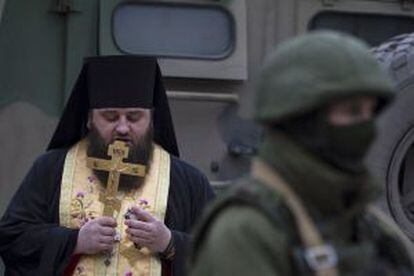 Un pope reza junto a un uniformado en Balaclava.