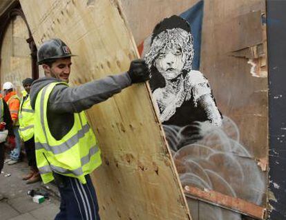 Un hombre cubre hoy con un tablón de madera el grafiti de Banksy ante la Embajada de Francia en Londres.