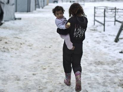 Una ni&ntilde;a siria camina con su hermana en brazos en el campo de Ritsona, en Grecia.