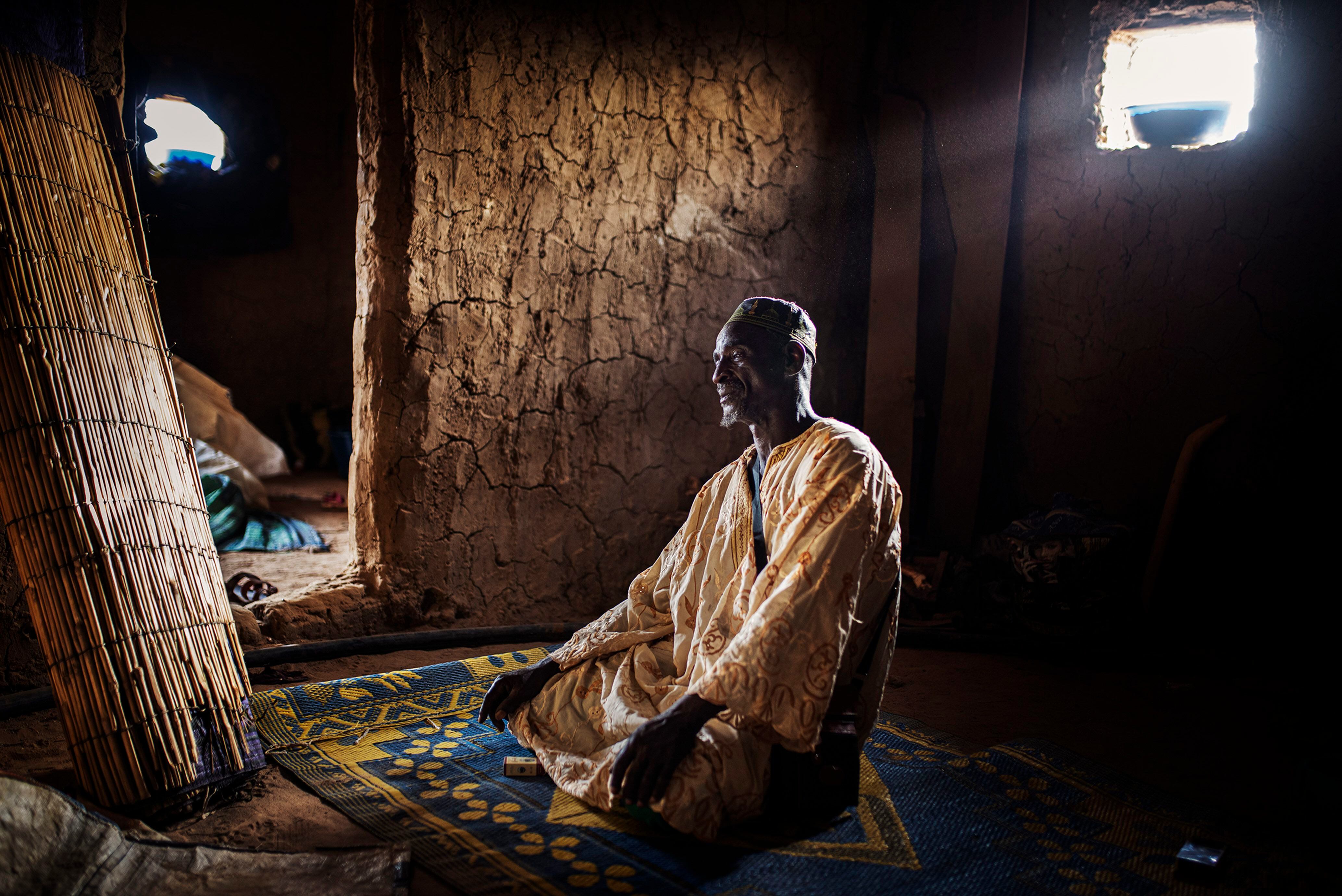 El comerciante de ganado Mahmoud Dicko reza en su nueva casa en la localidad de Dori, en el norte de Burkina Faso, después de abandonar su pueblo, Arbinda, a consecuencia de la violencia. Dicko se trasladó 80 kilómetros a pie durante tres días junto a una veintena de miembros de su familia. Hoy conviven todos en este pequeño espacio.