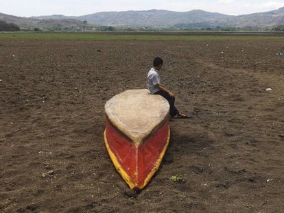Un niño permanece sentado sobre un bote en el terreno seco sobre el que estuvo el lago Atescatempa.