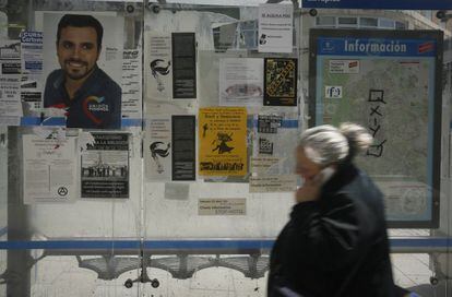 Una mujer habla por el móvil al pasar por una parada de autobús con un cartel del líder de IU Alberto Garzón que concurre en la coalición Unidos Podemos, en una calle de Madrid.