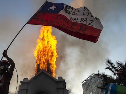 Un manifestante ondea una bandera chilena frente a una iglesia incendiada en Santiago, este domingo.