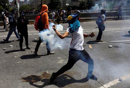 Un manifestante arroja un bidón de gas lacrimógeno a la policía.