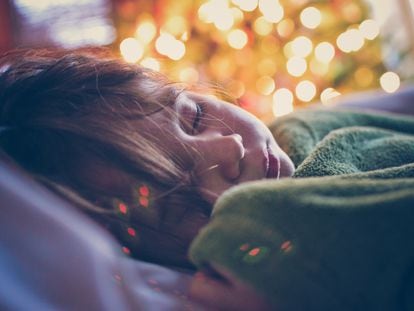 Una niña duerme junto a un árbol de Navidad.