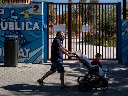 Un hombre pasa con un bebé esta mañana por la puerta del colegio Republica del Uruguay, en el distrito de Latina.